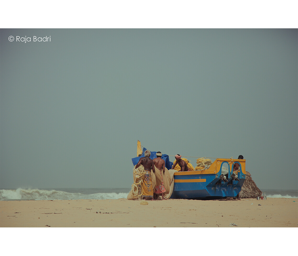 Fishermen hauling nets beside a wooden boat on the shore